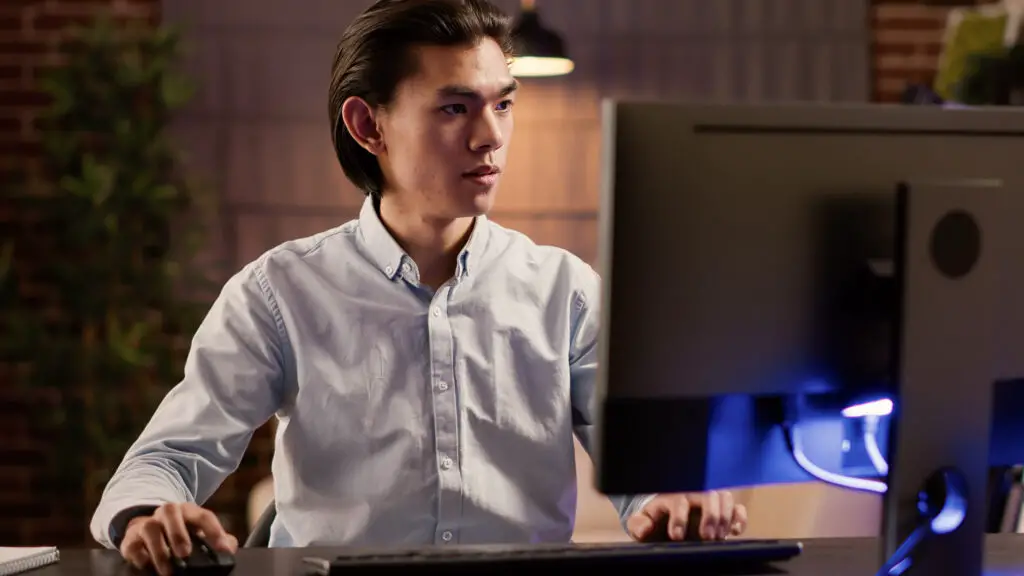 An Asian male data analyst focusing on analyzing data on the office desktop
