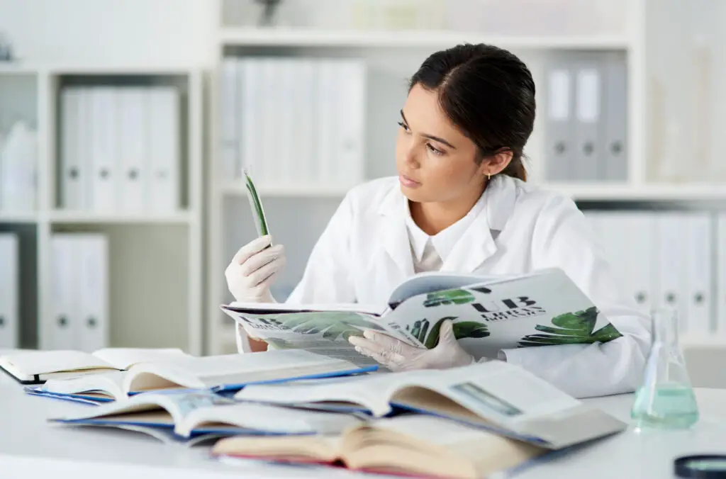 A female research assistant examines a specimen while books for reference inside a laboratory
