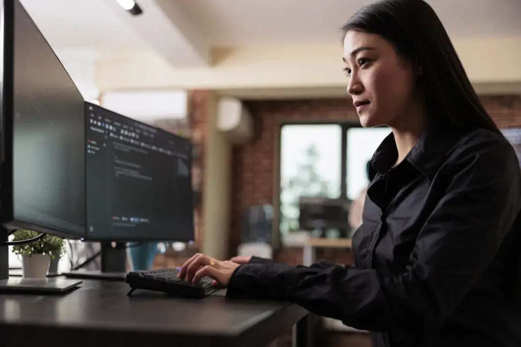 An Asian female software engineer focuses on coding on the office desktop