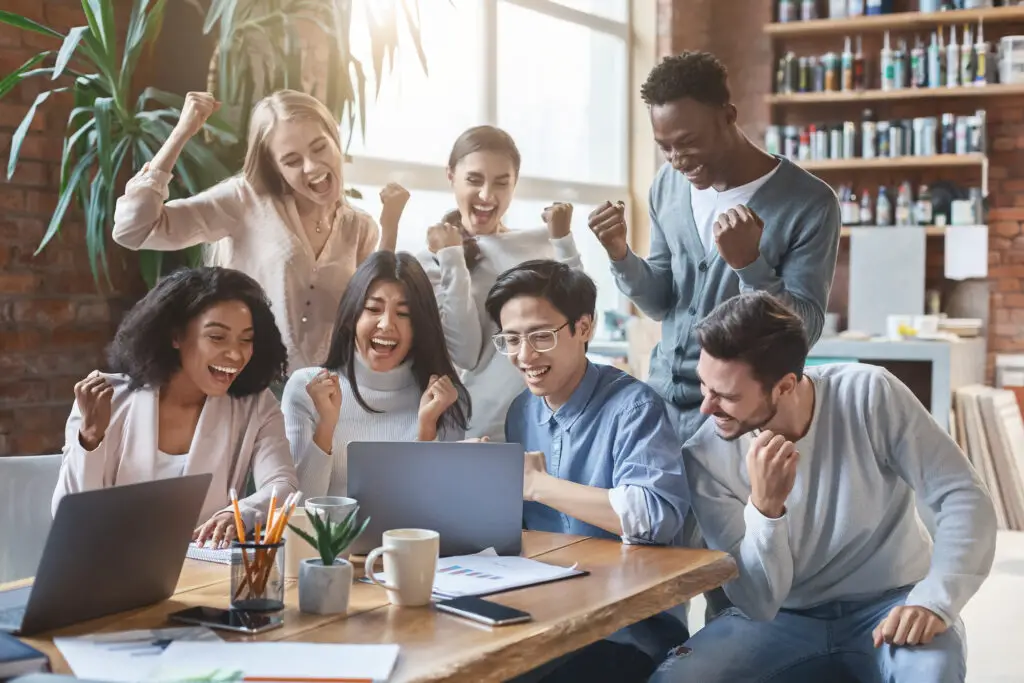 a group of male and female college students cheering while reading a successful college admission on a laptop screen