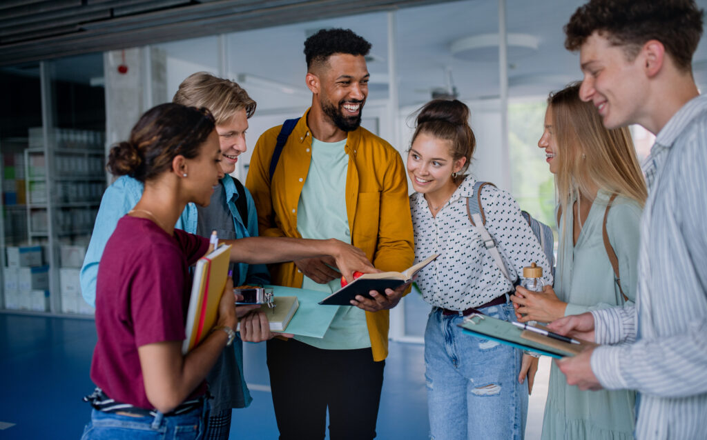 a diverse group of male and female college students holding books and a tablet while studying outdoors