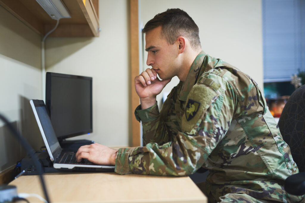 a male  college student in the military wearing a camouflage uniform is studying