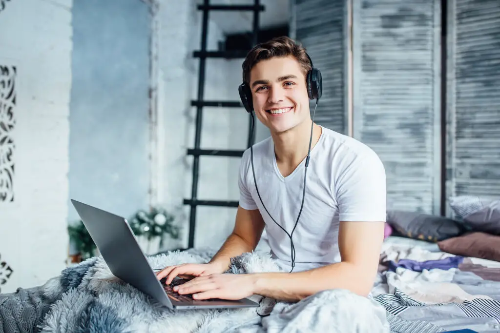 A smiling male high school graduate works on his online business while checking for updates about his online job