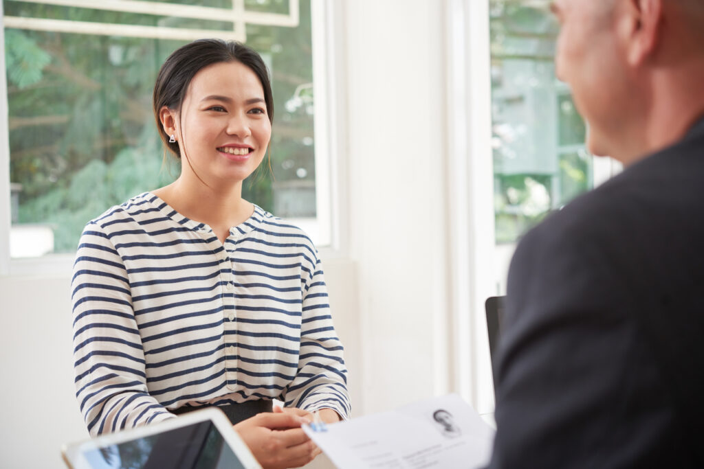 A smiling female college graduate answering a situational question to show critical thinking skills during her first job interview