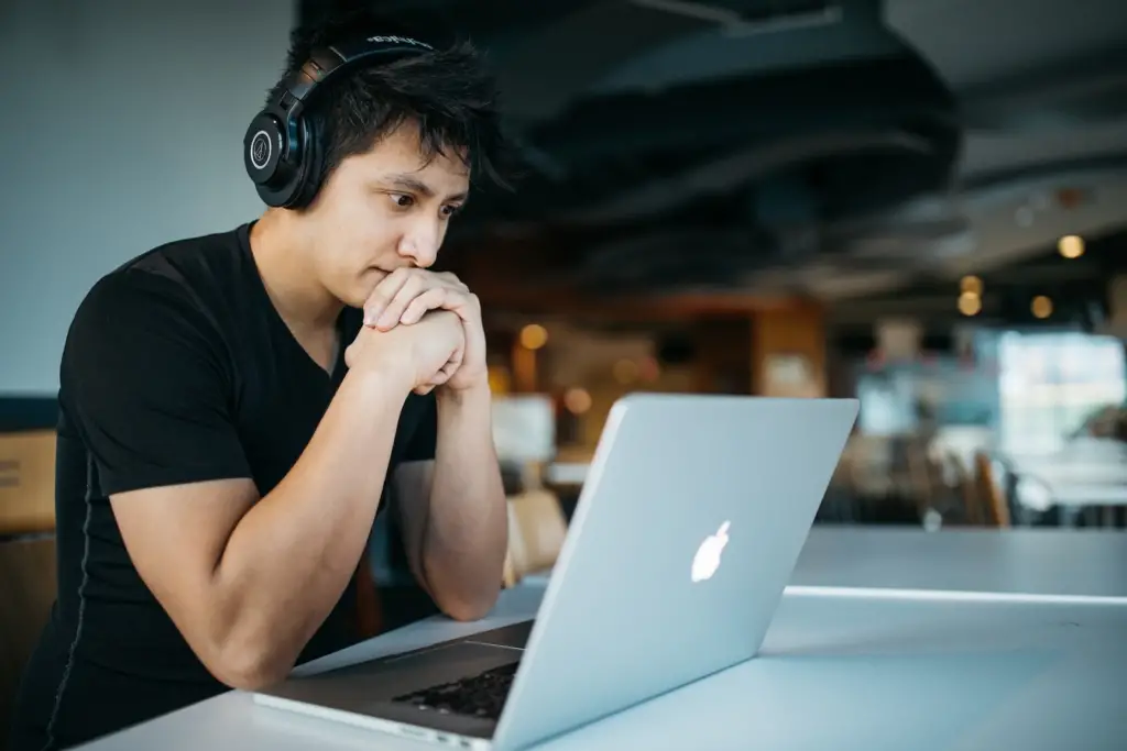 male student wearing headphones learning how to apply for college while looking at his college list on his laptop