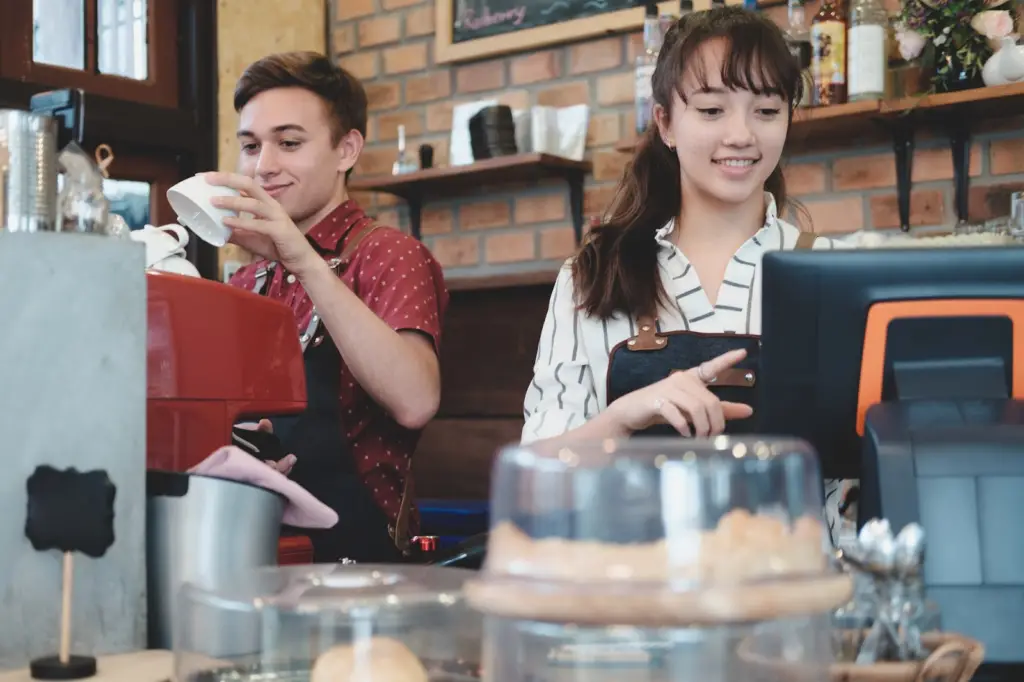 a male and female college student wearing aprons while working in a coffee shop as a free tuition deal with the employer
