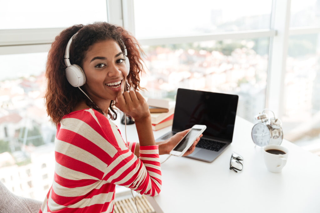 A smiling African-American fresh college graduate tests out different gadgets for a digital marketing job
