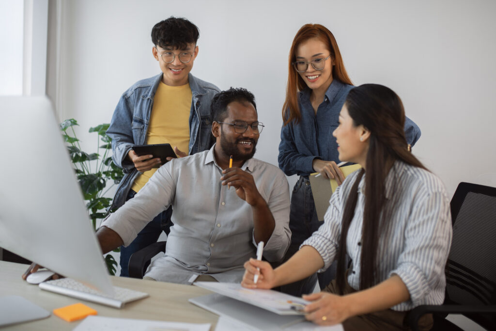 A multicultural group of four office professionals happily discussing a project collaboration 
