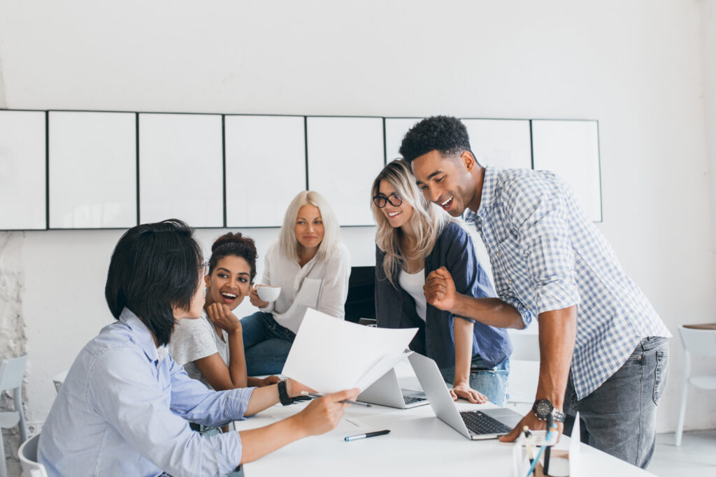 A diverse group of five young office workers happily discussing the good results of a project collaboration 