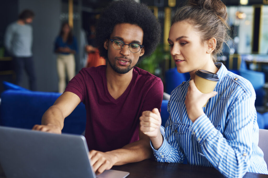 A female young professional holding her coffee listens to her male colleague explain the system of operations