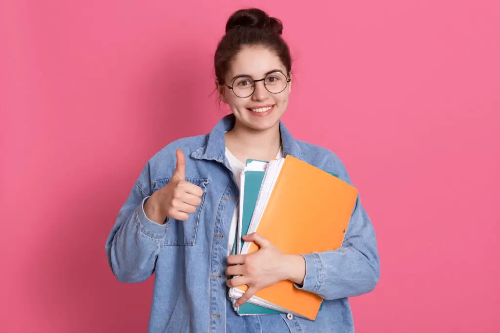 A smiling female incoming college freshman gives a thumbs up while holding the documentary requirements for different scholarship programs