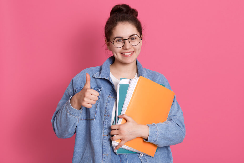 A smiling female incoming college freshman gives a thumbs up while holding the documentary requirements for different scholarship programs