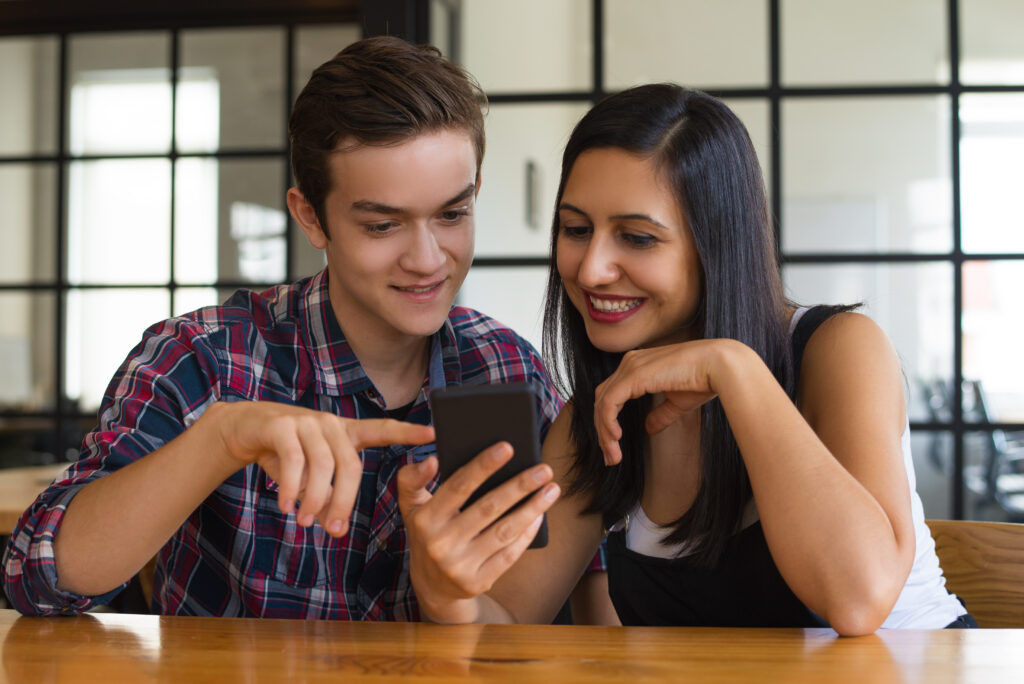 Two incoming college freshmen happily browse scholarship programs and tips on social media sites through their phone