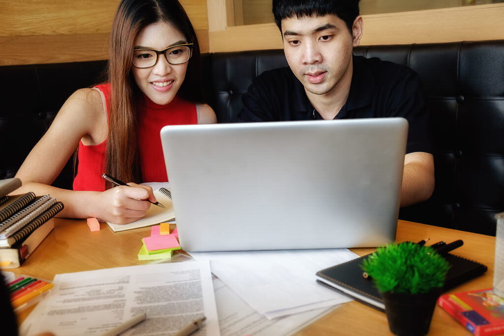 Two Asian college students search for scholarship news online on their laptop 