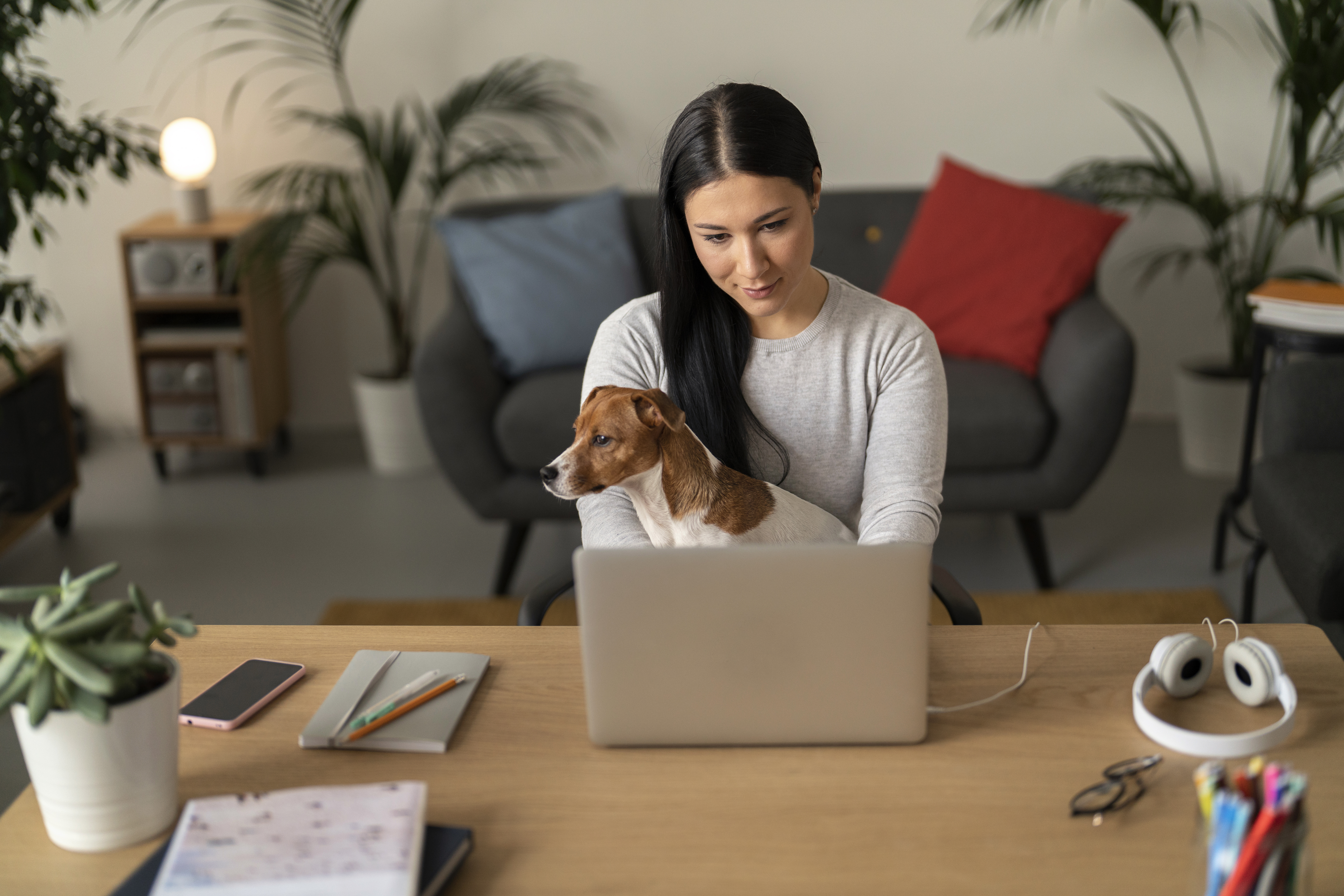 A female college student holds her small dog while attending an online class