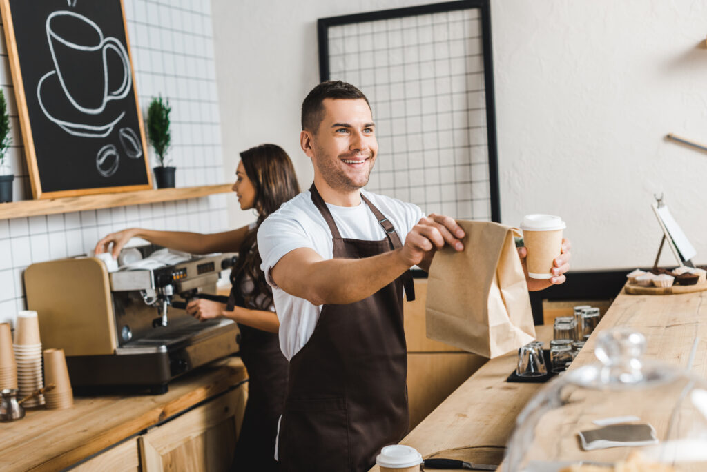 a male college student wearing an apron working as a part-time barista to help pay for college