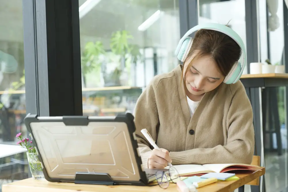 a female college student at home wearing headphones finding essay sources on digital libraries and databases using her laptop