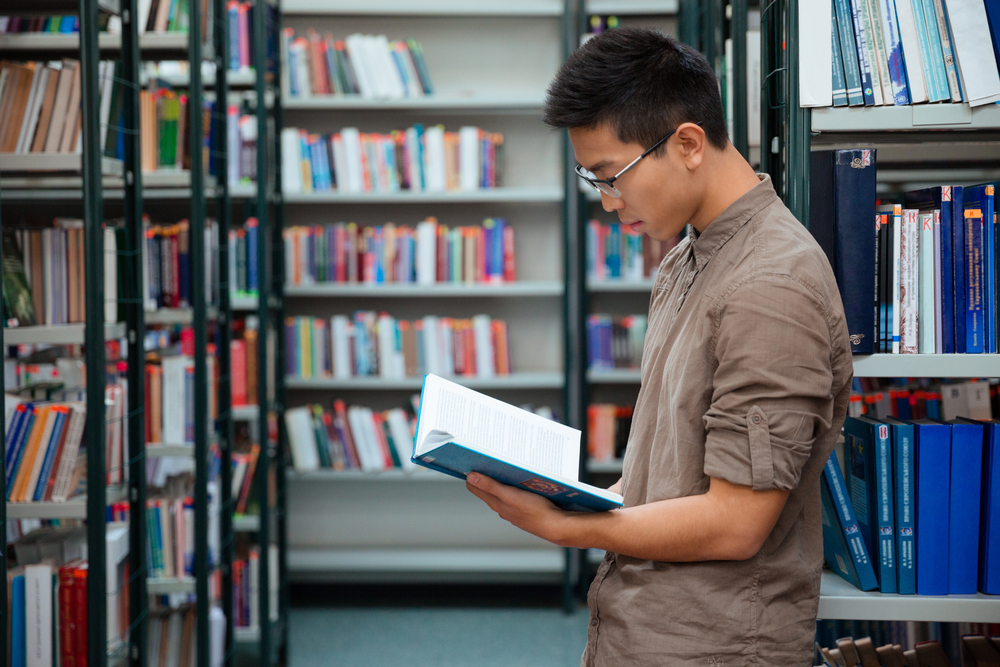 male college student finding essay sources inside the library