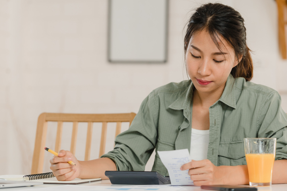 A smiling female student practicing how to budget and save money in college using her calculator and spreadsheets