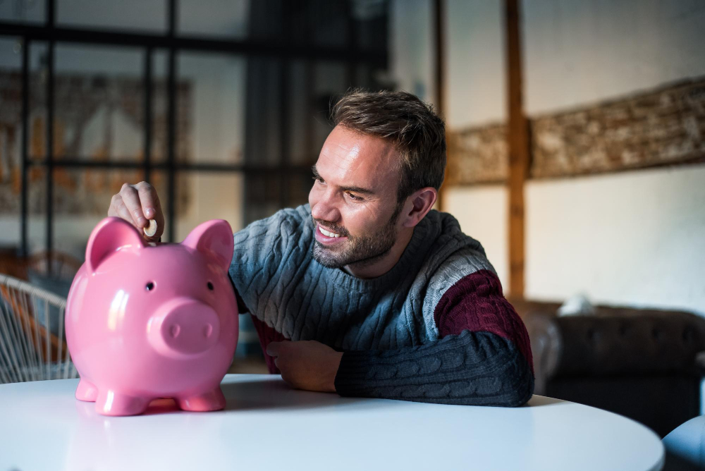 A smiling male college student fills his piggybank with coins as part of his budgeting practices
