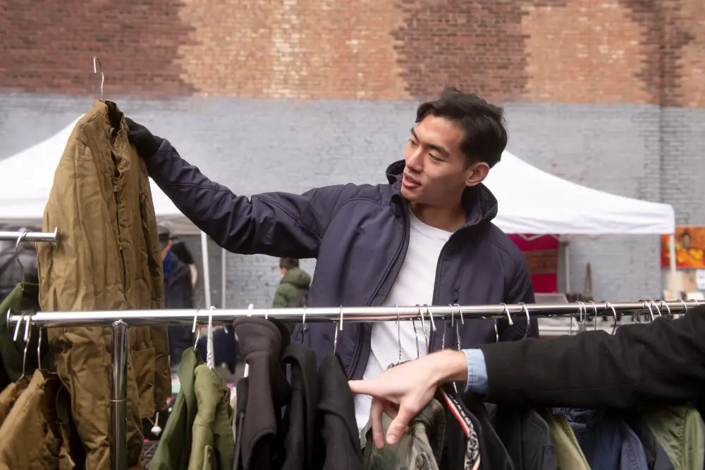 An Asian male college student shops for clothes on a budget as he checks out a jacket in a flea market