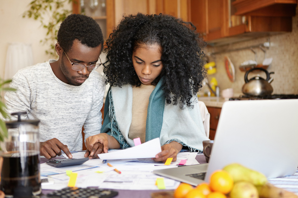 An African-American young couple calculates their college budget and expenses using credit card bills and receipts in their shared kitchen