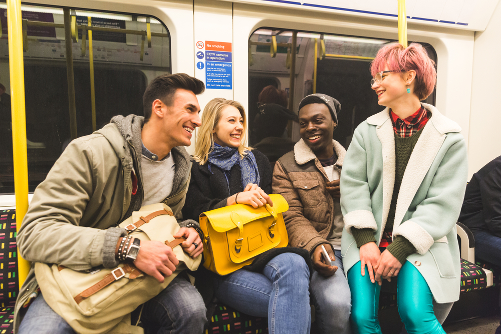 male and female college students sitting inside a subway train discussing college classes cost