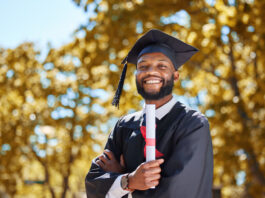 male college graduate wearing a diploma cap and gown proudly holding his diploma
