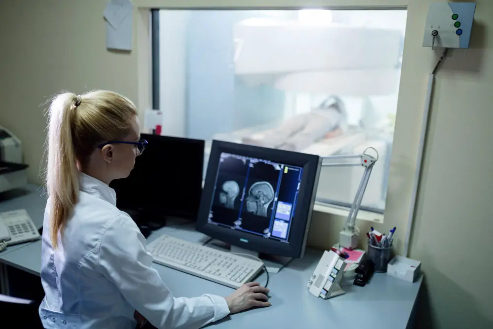A female radiologic and MRI technologist views a patient's brain scan on the computer
