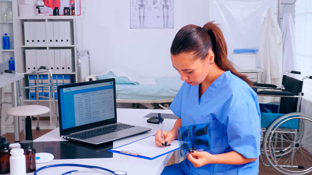 A female medical records specialist lists down information in both her paper report and digital database
