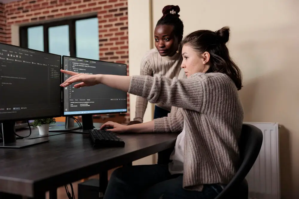 Two female software engineers discuss a coding project in an office  