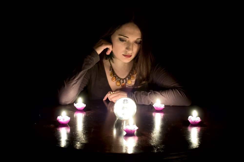 female college student staring at a crystal ball surrounded with candles