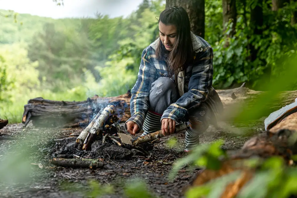 female college student learning how to start a fire outdoors in case of a zombie attack