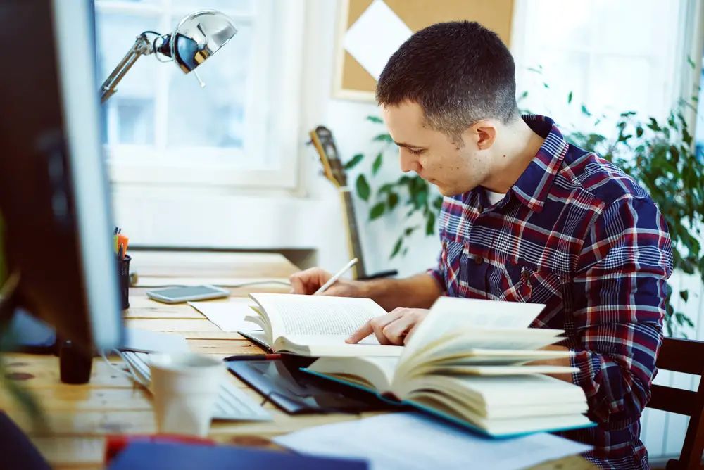 male college student reading books and completing an assignment