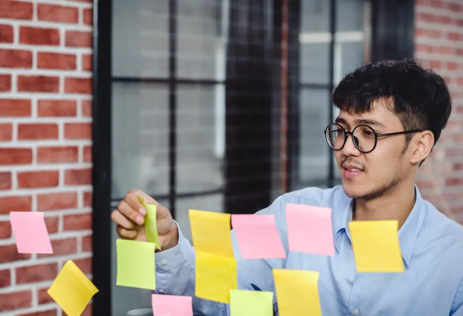 male college student looking and writing on sticky notes to track progress