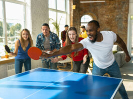 A group of four happy and energized students playing table tennis in one of the arcade college amenities
