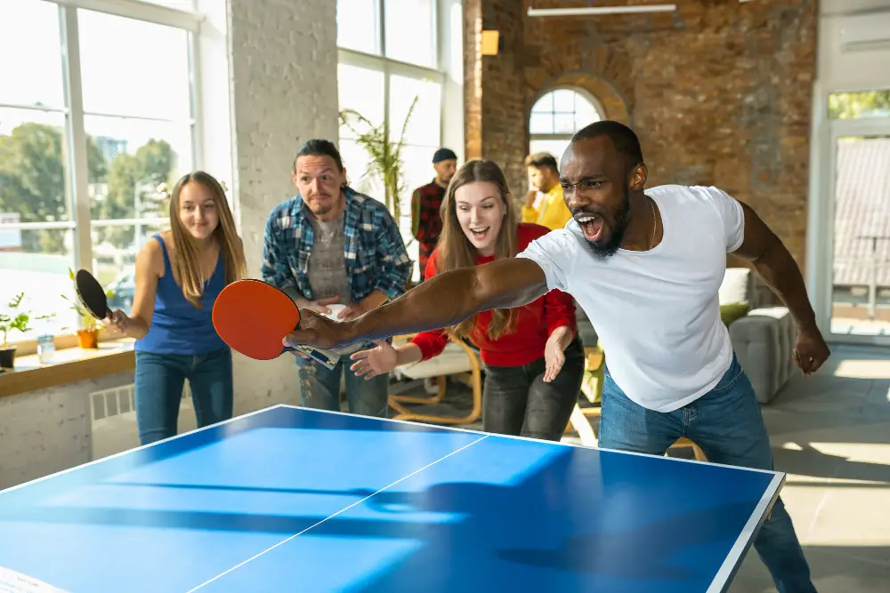 A group of four happy and energized students playing table tennis in one of the arcade college amenities