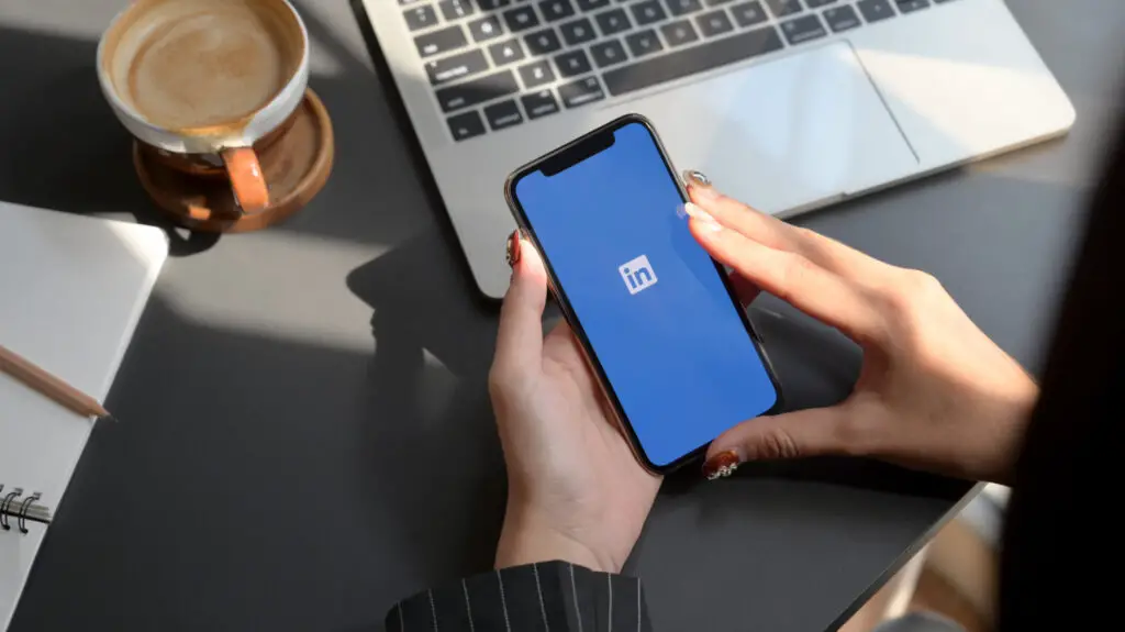 A female's manicured hands holding her phone with the LinkedIn logo on display