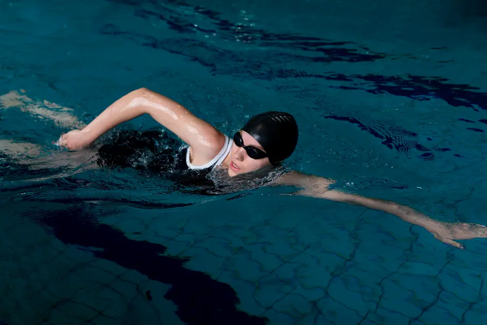 A female American college student wearing a cap and goggles swims in the university pool
