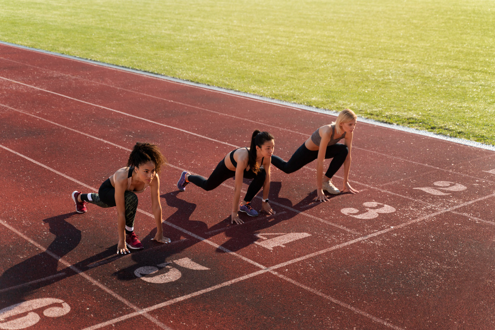 Three female college track and field athletes preparing to run at the starting line