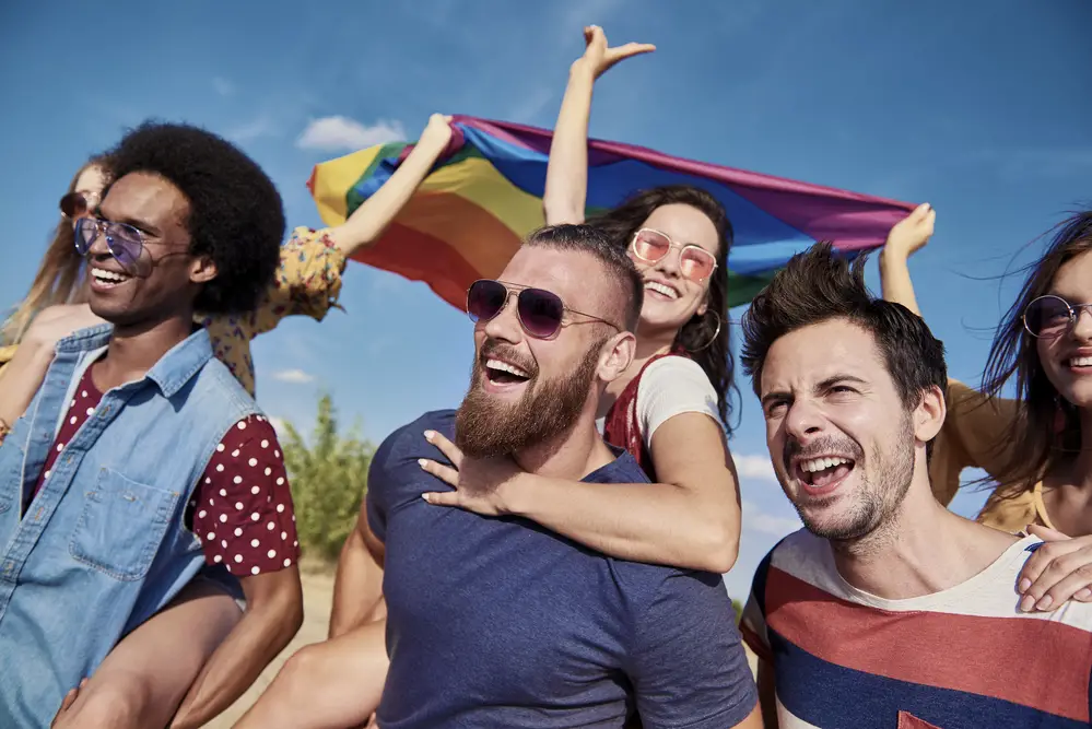 multiracial-group-of-friends-smiling-talking-to-each-other-outdoors-at-sunset-with-lgbtqi-flag