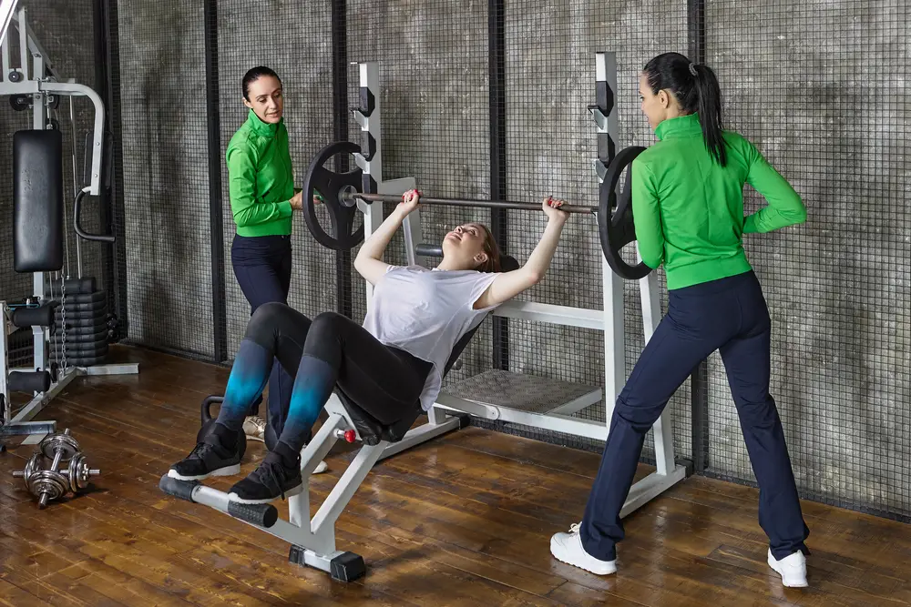 Female college students engaged in work-study programs as gym assistants help fellow female student with workout session