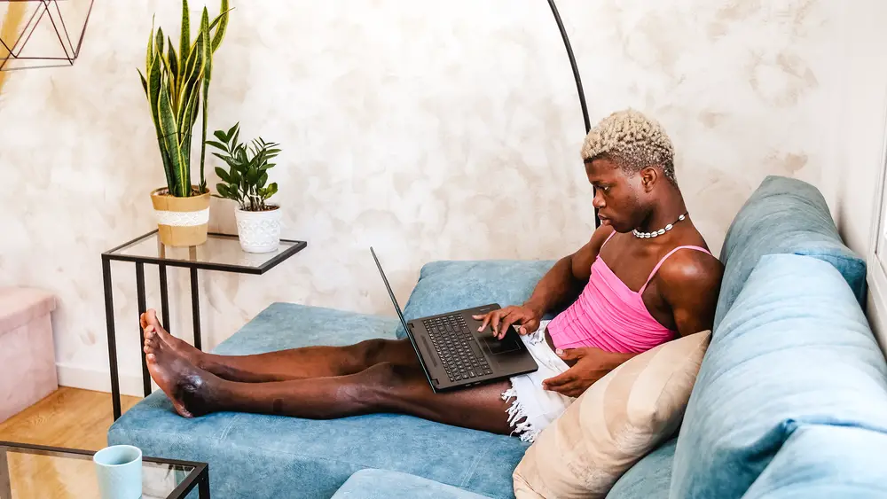 african-american-non-binary-person-in-feminine-clothes-working-on-laptop-in-their-room