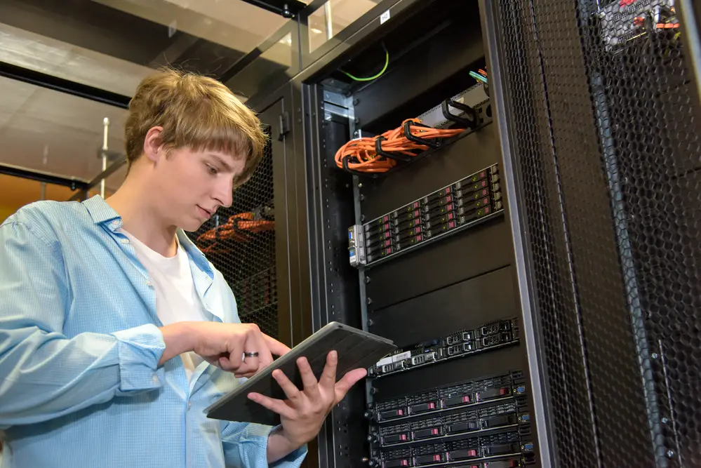Male college student engaged in a work-study program as an IT assistant checking the university server using a tablet