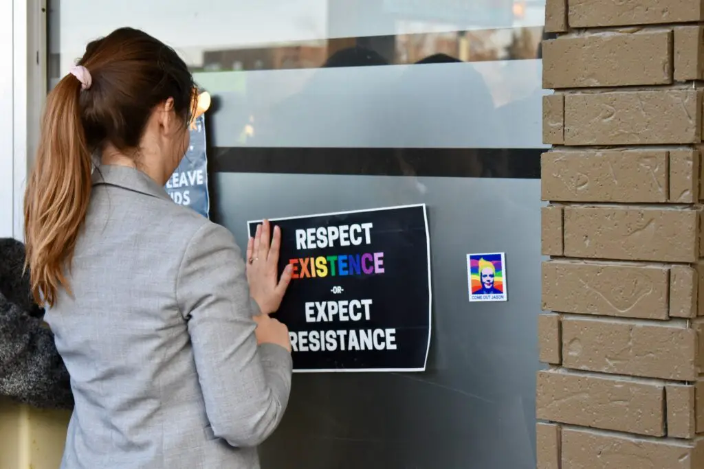 woman-in-formals-sticking-poster-about-respecting-lgbtq-existence-on-glass-door