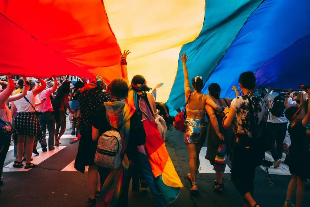 group of lgbt people under a giant lgbt flag at an event outdoors