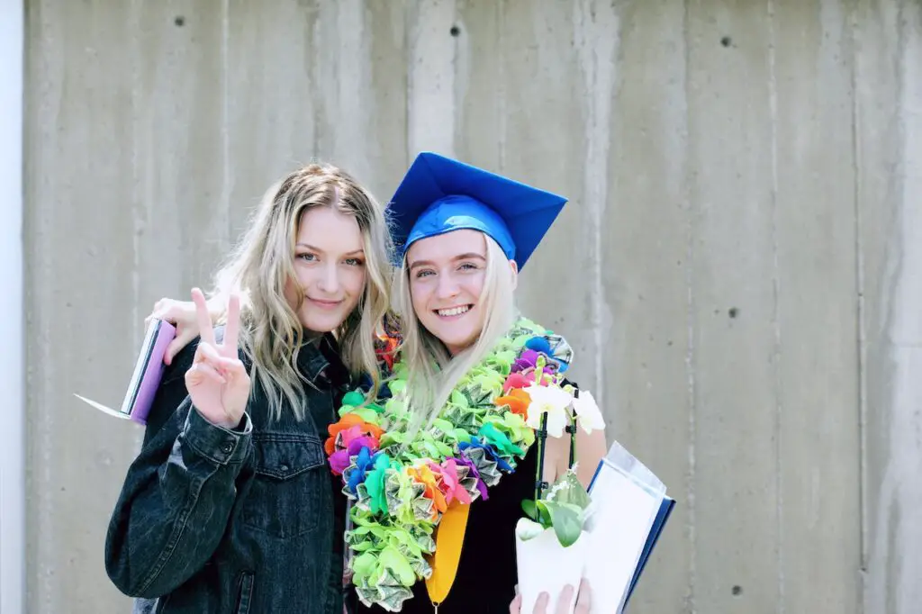 woman-wearing-graduation-cap-with-colorful-garland-standing-next-to-woman-in-blue-jacket