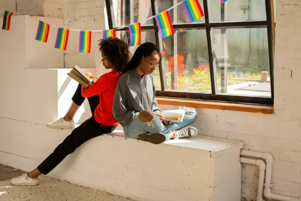 two-women-seated-on-window-pane-reading-book-together