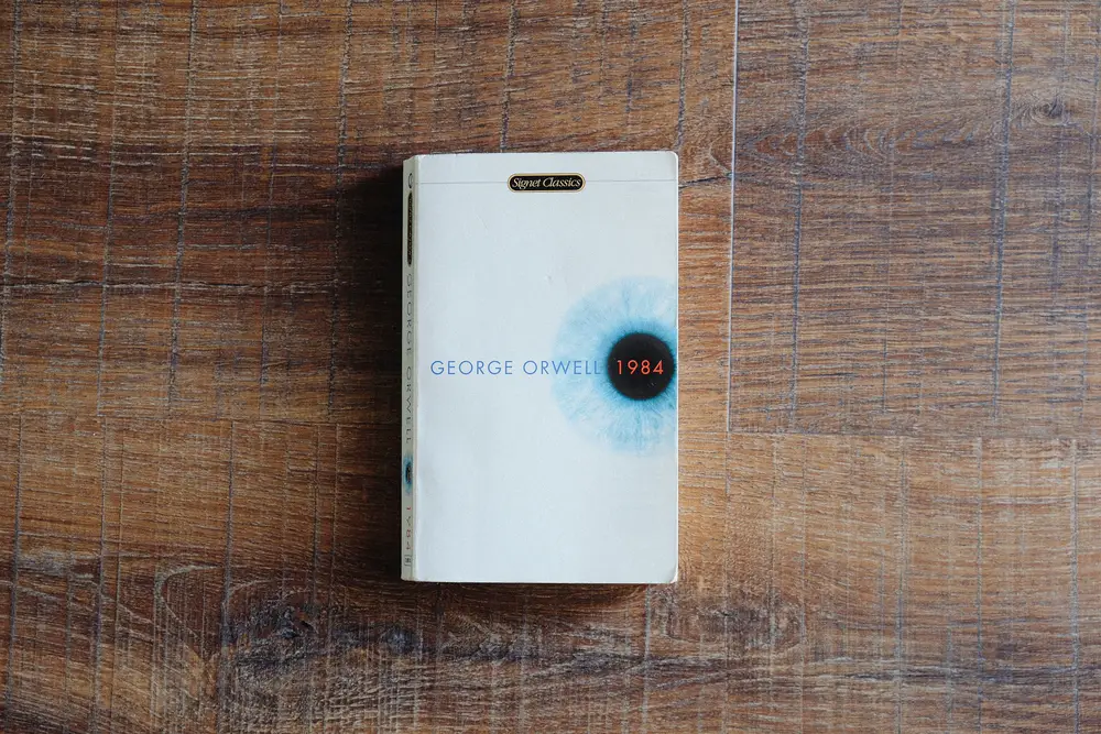 A paperback book of 1984 by George Orwell resting on a wooden table