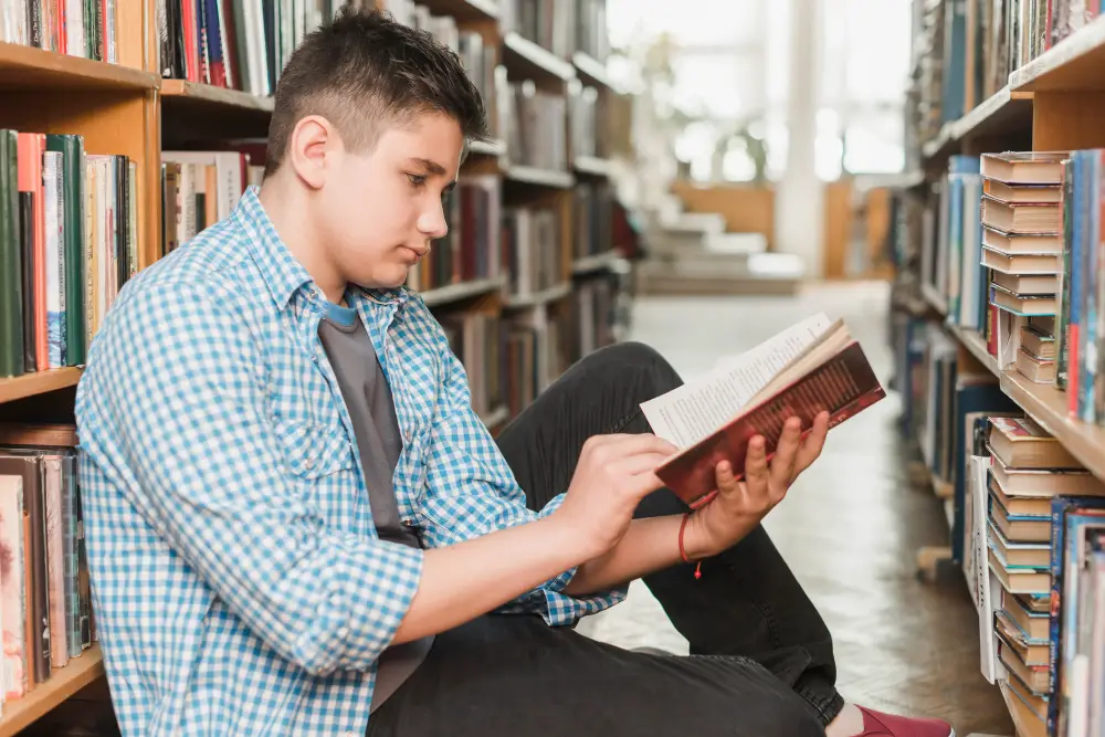 A male freshman reads one of the best books for college students he found in the library